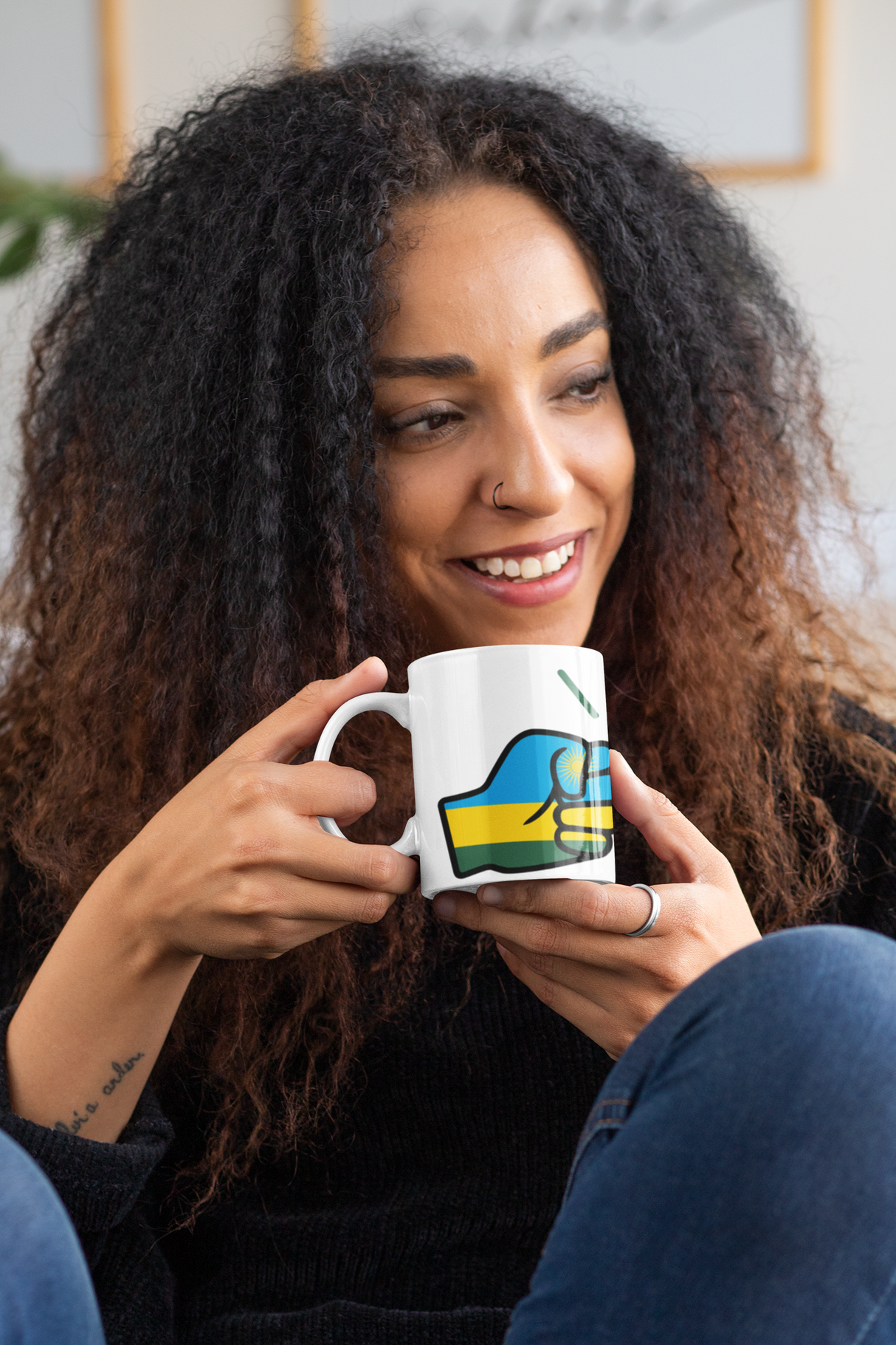 Woman holding a We Run Tings Rwanda tea, coffee mug, cup with a colorful design, sitting indoors.
