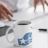 Black coffee in a white mug with the We Run Tings Somalia themed logo on a desk with a person using a computer in the background