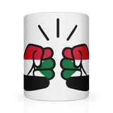 A glossy white ceramic We Run Tings, Sudan coffee, tea mug with a design of two fists on the side, representing the brand We Run Tings, and the flag of Sudan.