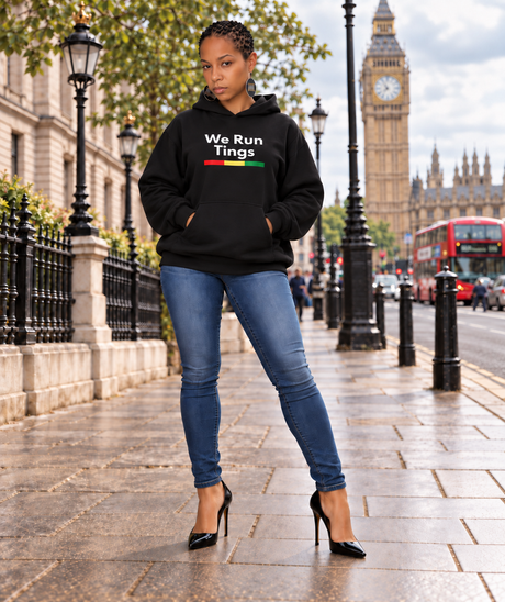 A woman stands on a London street wearing a black hoodie with the text 'We Run Tings' and a small red, yellow, and green stripe graphic. She is also wearing blue jeans and black high heels, with Big Ben and red double-decker buses in the background.