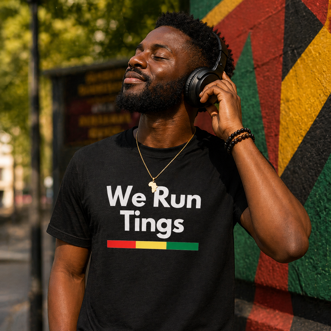 Man wearing a black t-shirt with 'We Run Tings' text, listening to music with headphones against a colorful wall.