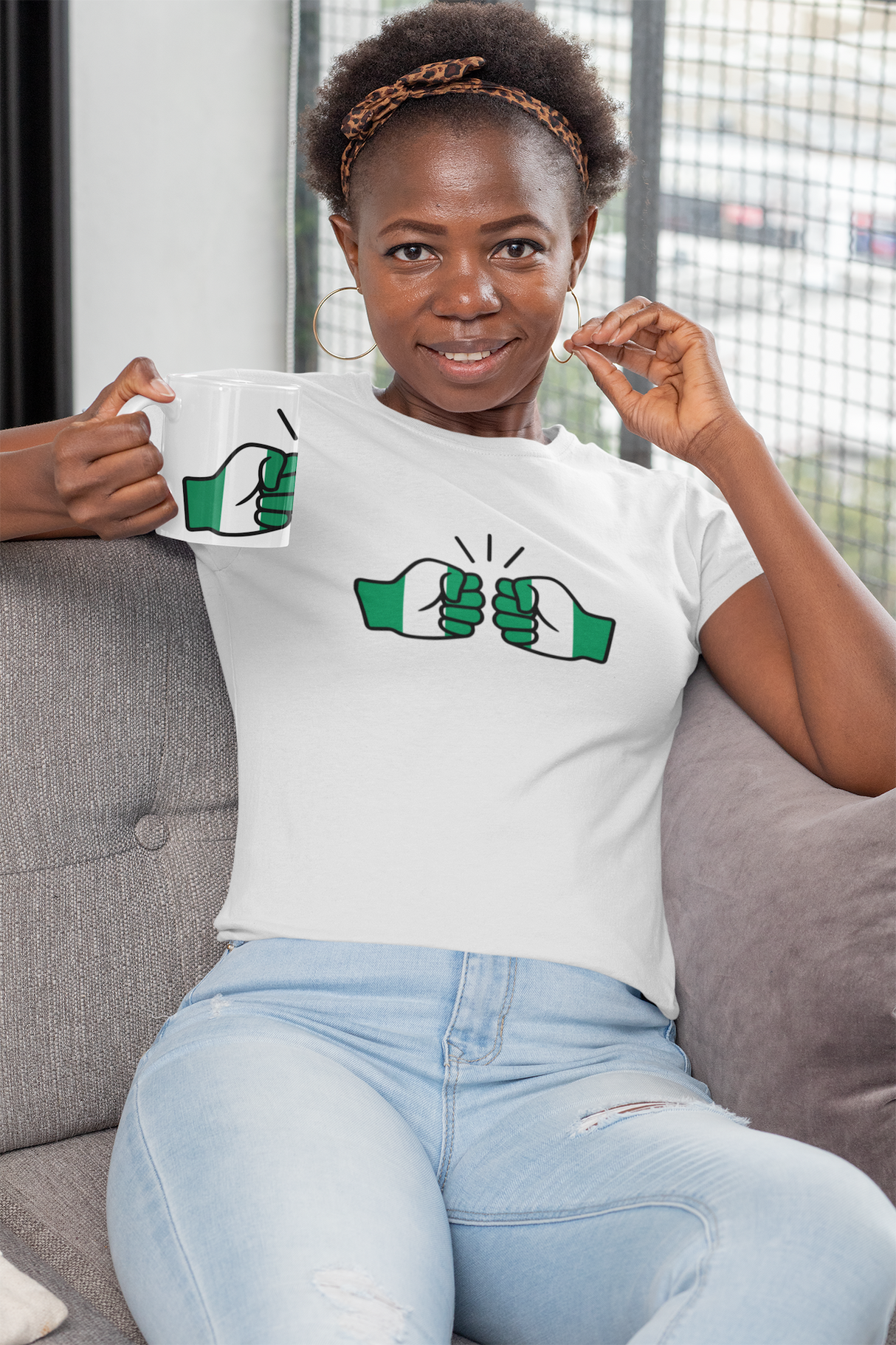 Woman holding a We Run Tings Nigerian themed white ceramic tea, coffee, mug, cup and matching branded t-shirt with a design on a couch